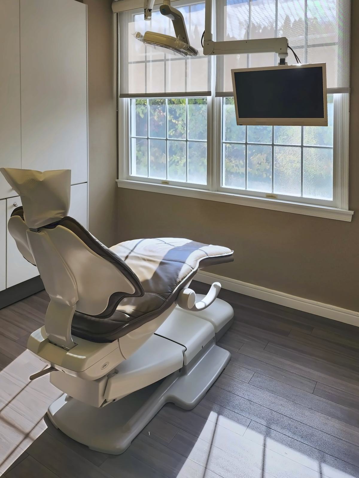 A treatment room at Sora Dentistry with a dental chair, an overhead light, and a window onto trees