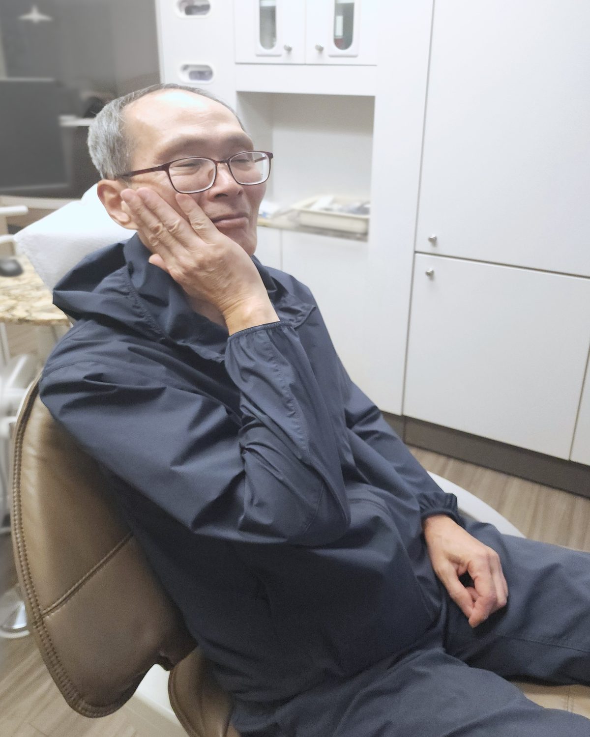 A man in a dental chair holding his cheek, as if he has a toothache