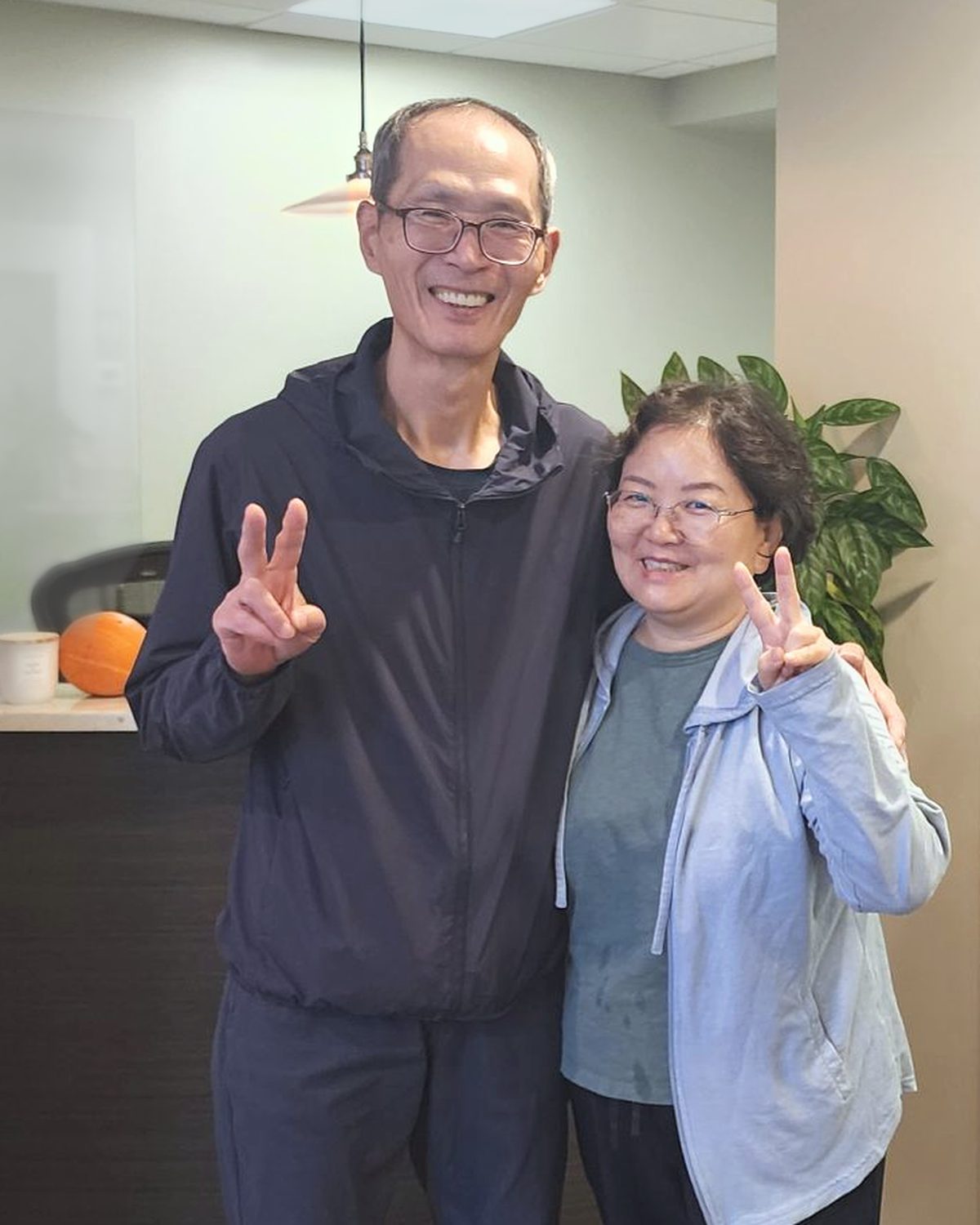 Two smiling adults standing together in the reception area of the office, each making a peace sign.